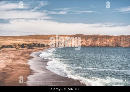 Ein atemberaubender Blick auf Playa Roja, bekannt für seinen einzigartigen roten Sand und die dramatischen Klippen im Paracas Natural Reserve. Stockfoto
