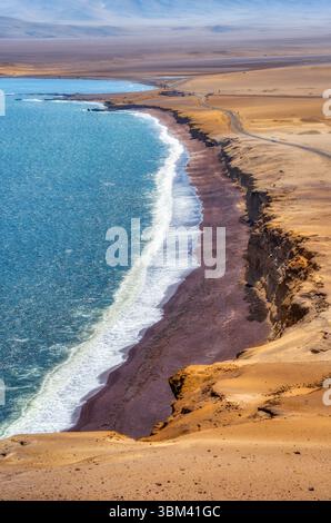 Ein atemberaubender Blick auf Playa Roja, bekannt für seinen einzigartigen roten Sand und die dramatischen Klippen im Paracas Natural Reserve. Stockfoto