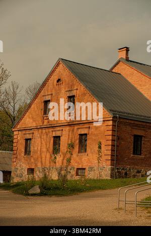 Ein gut erhaltenes historisches Backsteingebäude mit Giebeldach, fotografiert in sanftem Abendlicht. Das Gebäude verfügt über Grundmauern aus Stein. Stockfoto