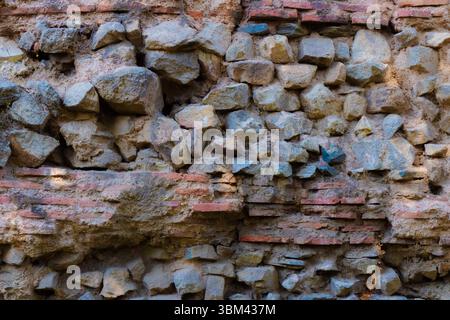 Dieses Gebäude verfügt über eine alte Steinmauer aus verwitterten Ziegeln und unregelmäßigen Steinen, die den Verlauf der Zeit in einer historischen Umgebung widerspiegelt. Stockfoto