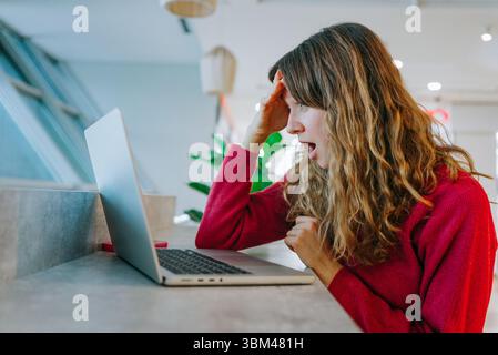 Professionelle Frau, die während eines Videoanrufs beim Betrachten des Laptops Schock zeigt und in einer modernen Büroumgebung unerwartete Kommunikation am Arbeitsplatz erlebt Stockfoto