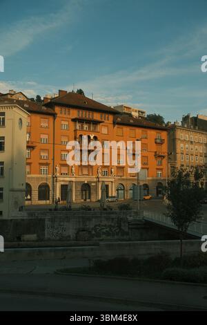 Dieses markante orangene Gebäude, das in das goldene Licht des späten Nachmittagslichts getaucht ist, steht stolz an einer europäischen Straße. Stockfoto