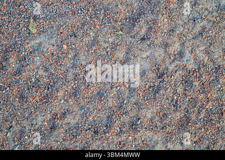 Detaillierter Hintergrund des verdichteten Bodens, der mit kleinem Kies und Sand bedeckt ist. Natürliche Oberflächenstruktur mit einer Mischung aus orangen und blauen Steinen, ideal für uns Stockfoto