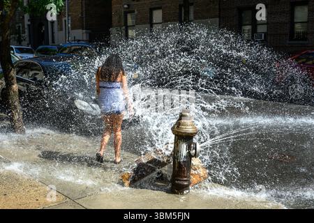 New York, USA. Juni 2025. Kinder spielen mit einem Wasserstrahl aus einem offenen Hydranten im Viertel Washington Heights in Manhattan während einer Hitzewelle mit Temperaturen bis zu 99 °F (über 37 °C). Quelle: Enrique Shore/Alamy Live News Stockfoto