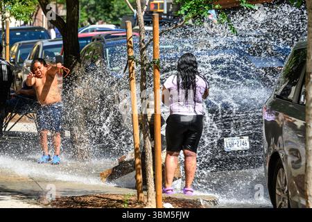 New York, USA. Juni 2025. Kinder spielen mit einem Wasserstrahl aus einem offenen Hydranten im Viertel Washington Heights in Manhattan während einer Hitzewelle mit Temperaturen bis zu 99 °F (über 37 °C). Quelle: Enrique Shore/Alamy Live News Stockfoto