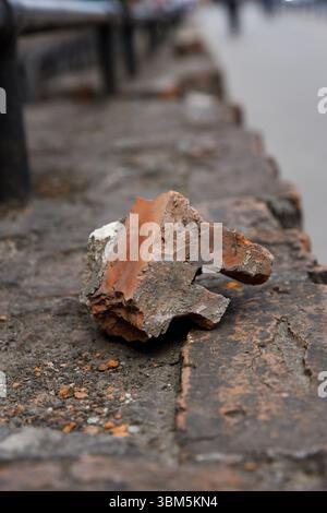 Dieses Bild zeigt eine Nahaufnahme eines verwitterten Ziegelfragments zwischen Steinen, das die natürlichen Strukturen des urbanen Verfalls und der Zeitlosigkeit hervorhebt Stockfoto
