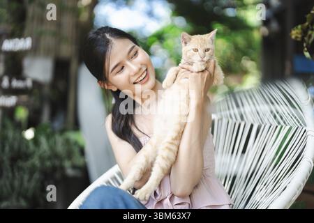 Lächelnde schöne asiatische junge Frau mit Ingwerkatze Wellness-Porträt Glück im Freien Stockfoto
