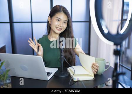 Glückliche junge Frau macht Audio-Podcast im Studio asian Woman, die Podcast auf Tablet mit Kopfhörern und Mikroskop für Online-Streaming aufnimmt Stockfoto