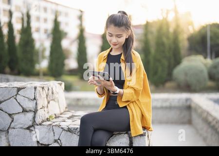 Lächelnde junge asiatische Frau mit digitalem Tablet in der Stadt Stockfoto