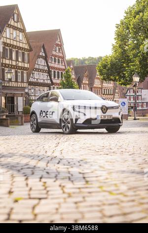 Ein weißes Auto parkt auf einem Kopfsteinpflasterplatz mit charmanten Fachwerkhäusern im Hintergrund, Deer E, Carsharing, Elektroauto, Calw, Schwarzwald Stockfoto