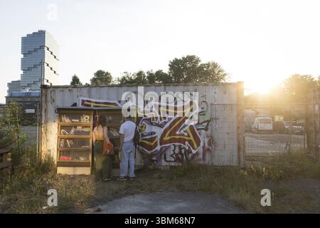 Zwei Personen stehen vor einem Bücherschachtel auf dem ROHGELÄNDE vor der untergehenden Sonne mit Edge Tower (Amazonasturm) im Hintergrund, Berlin, 21/06 Stockfoto