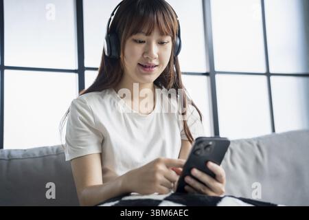 Asiatische Frau, die Musik hört, Podcast entspannt auf dem Sofa Stockfoto