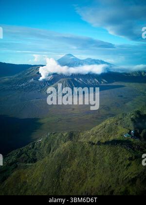 Rauch und Dampf kommen vom Berg Bromo (Gunung Bromo) mit dem Berg Semeru in der Ferne, Ost-Java, Indonesien - aus der Luft Stockfoto