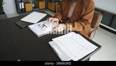 Asiatische Frau mittleren Alters Wirtschaftsprüfer oder interne Einnahmen Service leitende Geschäftsfrau überprüft jährliche finanzielle ältere Frau Drücken Rechner Stockfoto