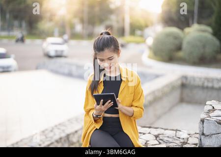 Lächelnde junge asiatische Frau mit digitalem Tablet in der Stadt Stockfoto