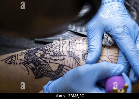 Nahaufnahme der Hände eines Mannes, der in einem Tattoo-Studio das Bein einer Frau auf einer Bahre tätowiert Stockfoto