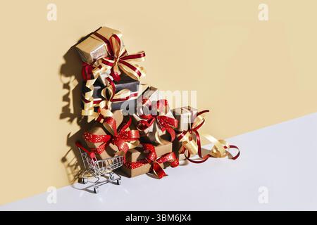 Warenkorb mit Geschenkboxen auf beige grauem Hintergrund. Geschenke verpackt in Kraftpapier mit Band und Schleife. Holiday Shopping-Konzept Stockfoto