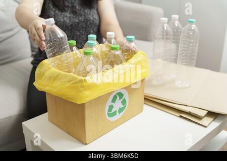 Recyceln Sie die umweltfreundliche Zero Concept Frau, die leere Plastikflasche mit gelben Mülltüten zu Hause in den Recyclingbehälter wirft Stockfoto