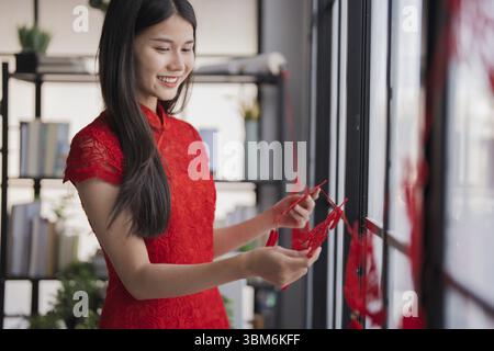 Schöne junge asiatische Frau rote Kleidung macht Papier Handwerk rot chinesische Neujahrs Laterne für Lunar Neujahrsdekorationen Chinesische Neujahrsfeiern f Stockfoto
