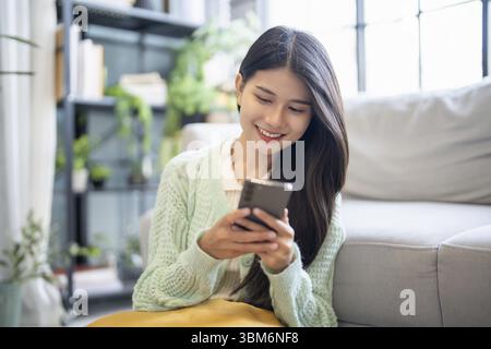 Asiatische Frau mit Sprachassistent auf Smartphone zu Hause Gespräch mit Online-Assistent Sprachchatbot Konversation AI Moderne Technologien Stockfoto