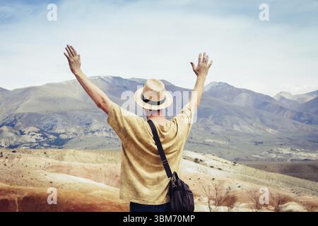 Männlicher Tourist mit offenen Händen steht auf einem Berg und blickt auf eine Bergkette Stockfoto