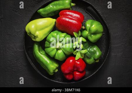 Verschiedene rote und grüne Paprika mit Wassertropfen auf schwarzem Hintergrund Stockfoto