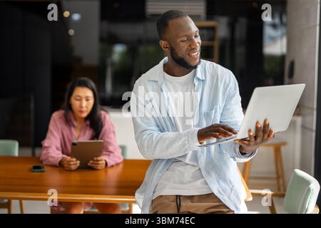 Schwarzer Afroamerikaner, der sein Online-Banking, sein soziales Leben und seine Aufgaben auf einem Laptop verwaltet Stockfoto