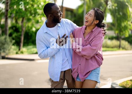 Glückliches, interrassisches Paar lacht zusammen draußen, genießt einen unbeschwerten Moment der Liebe, Freude Stockfoto