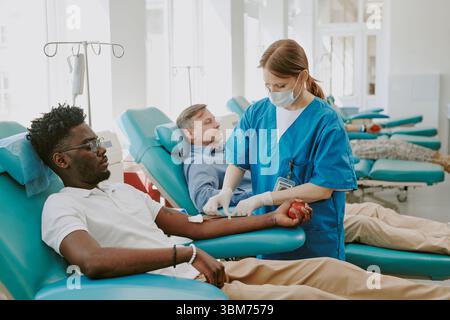 Junger Schwarzer und kaukasischer Mann mittleren Alters spenden Blut in der Klinik Stockfoto