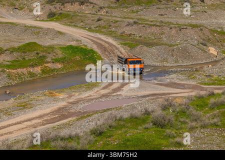 Lkw mit Felsbrocken, der durch den Fluss in ländlichen Bergregionen fährt Stockfoto