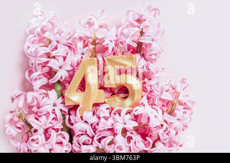 Nummer 45 fünfundvierzig goldene Geburtstagskerze auf rosa Blumen Hintergrund. 45 Jahre Geburtstag. Das Konzept, Geburtstag, Jahrestag zu feiern, ich Stockfoto