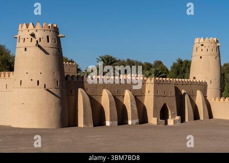 Eine Festung mit Zinnen und zwei runden Türmen steht unter einem klaren blauen Himmel im Al Jahili Fort in Al Ain Vereinigte Arabische Emirate. Stockfoto