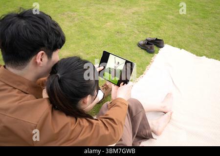 Ein junges chinesisches Paar, das sich umschließt, während er sich Bilder auf einem Tablet ansieht Stockfoto
