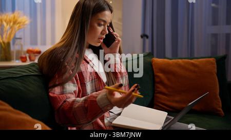 Kaukasische Multitasking Frau studiert Talk Handy schreibt Notizen zu Hause Abend online Arbeit Geschäftsfrau Studentin Teenager Mädchen mit Laptop Stockfoto