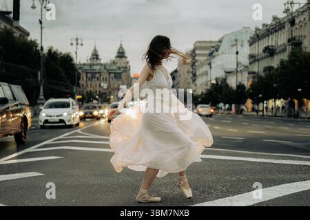Eine Frau in fließendem Kleid tanzt anmutig mitten in einer Stadtstraße und bringt Bewegung und Leben in die städtische Umgebung. 18. Mai 2024, Kiew, Khre Stockfoto