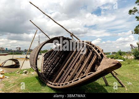 Ein verwittertes Holzboot liegt kopfüber neben einem Fluss, umgeben von Gras und Trümmern. Stockfoto