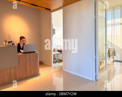 Junge Frau in einem modernen Empfangsbereich k, die in einer laptop.in Klinik, einem Spa, Schönheitssalon, Wellness-Klinik oder ähnlichen serviceorientierten Räumen arbeitet Stockfoto