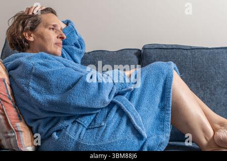 Eine Frau im Gewand liegt auf einer blauen Couch. Sie trägt ein blaues Gewand und hat ihren Kopf an der Hand Stockfoto