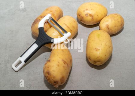 Eine Sammlung frischer Kartoffeln, die ordentlich neben einem Kartoffelschäler auf einer Küchenfläche angeordnet sind Stockfoto