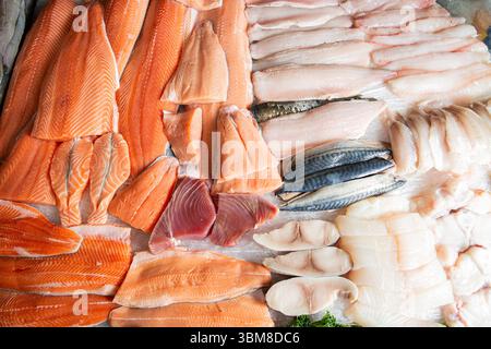 Overhead-Ansicht verschiedener roher Fischfilets - Lachs, Forelle, Thunfisch, Makrele - auf einem Markttheken. Saubere Schnitte, frische Meeresfrüchte. Stockfoto