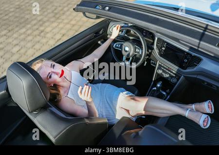 Selbstbewusste junge Frau im weißen Cabriolett, Beine auf dem Armaturenbrett Stockfoto