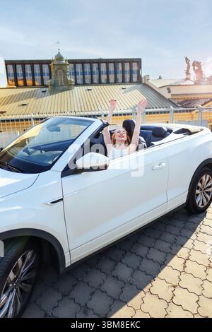 Stilvolle junge Frau, die an einem sonnigen Tag in der Stadt im Cabrio lächelt. Stockfoto