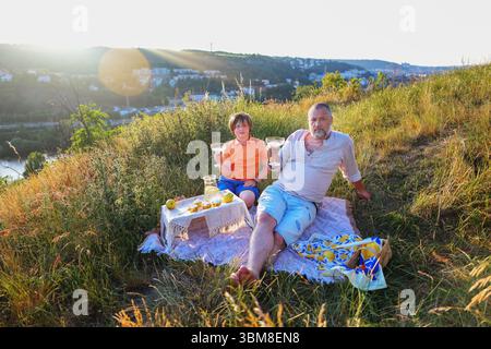 Vater und Sohn genießen ein Sommerpicknick mit Obst und Limonade auf einem sonnigen Hügel Stockfoto