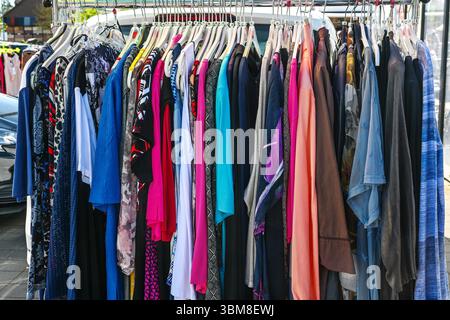 Farbenfrohe gebrauchte Kleidung, die an einem Regal zum Verkauf auf einem Flohmarkt an einem sonnigen Tag hängt, ausgewählter Fokus, enge Schärfentiefe Stockfoto