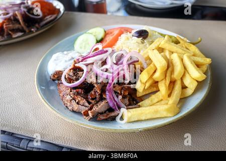 Gyros mit Pommes frites, Zwiebeln, Krautsalat, Salat und Tzatziki auf einem Teller in einem griechischen Straßenrestaurant, mediterranes Fast Food, Kopierraum, ausgewählt f Stockfoto