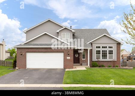 Ein zweistöckiges Einfamilienhaus in einem Vorort mit grauem Vinyl und rotem Backsteinfeld und zwei Garagen. Stockfoto
