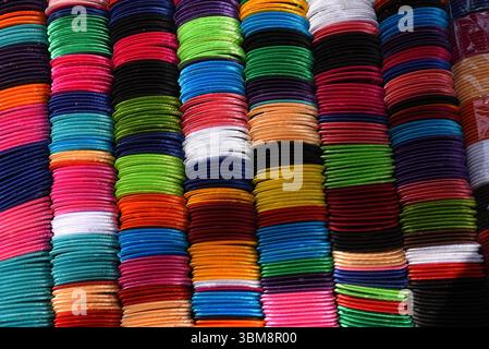 Ein lebendiges und symmetrisches Muster traditioneller Armreifen in verschiedenen Farben, ordentlich in Reihen angeordnet. Diese Armreifen, oft aus Glas und Metall. Stockfoto