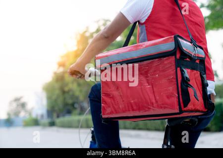 Junger männlicher Lieferradfahrer, der Teilzeit arbeitet und mit einem Lebensmittelrucksack durch die Straßen der Stadt fährt. Stockfoto