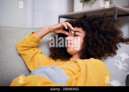 Junge Frau, die sich in lässiger Kleidung zu Hause gestresst auf einer Couch entspannt Stockfoto