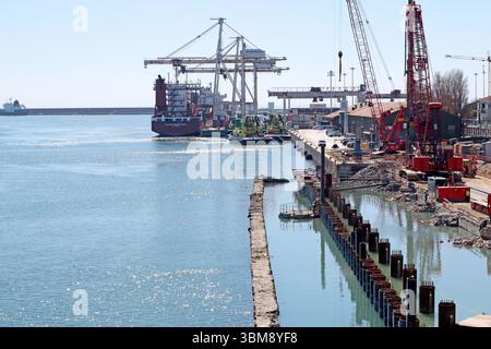Städtische Baustelle mit sichtbarem Gerüst, Betonbarrieren und Fundamentarbeiten. Krane, Stützstrukturen und Teilansicht des nahegelegenen Gebäudes Stockfoto